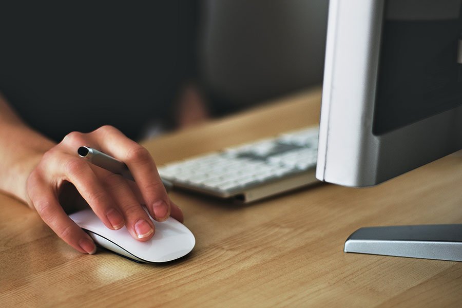A computer keyboard and mouse with hand on it.